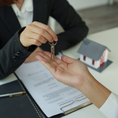 real estate agent holding house key to his client after signing contract agreement in office,concept for real estate, moving home or renting property.